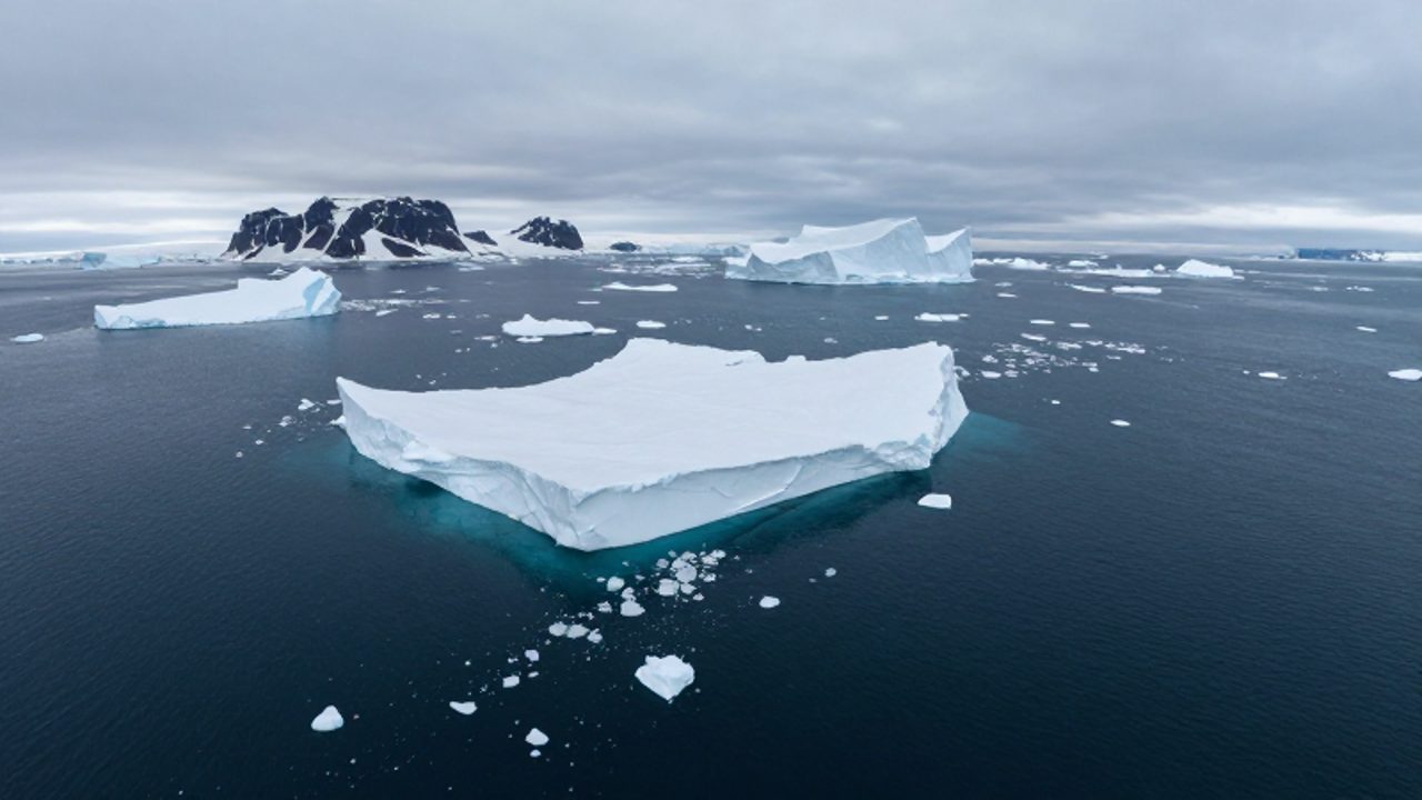 Vista aérea de un vasto océano ártico con grandes bloques de hielo flotando sobre aguas oscuras cerca de una costa gélida.