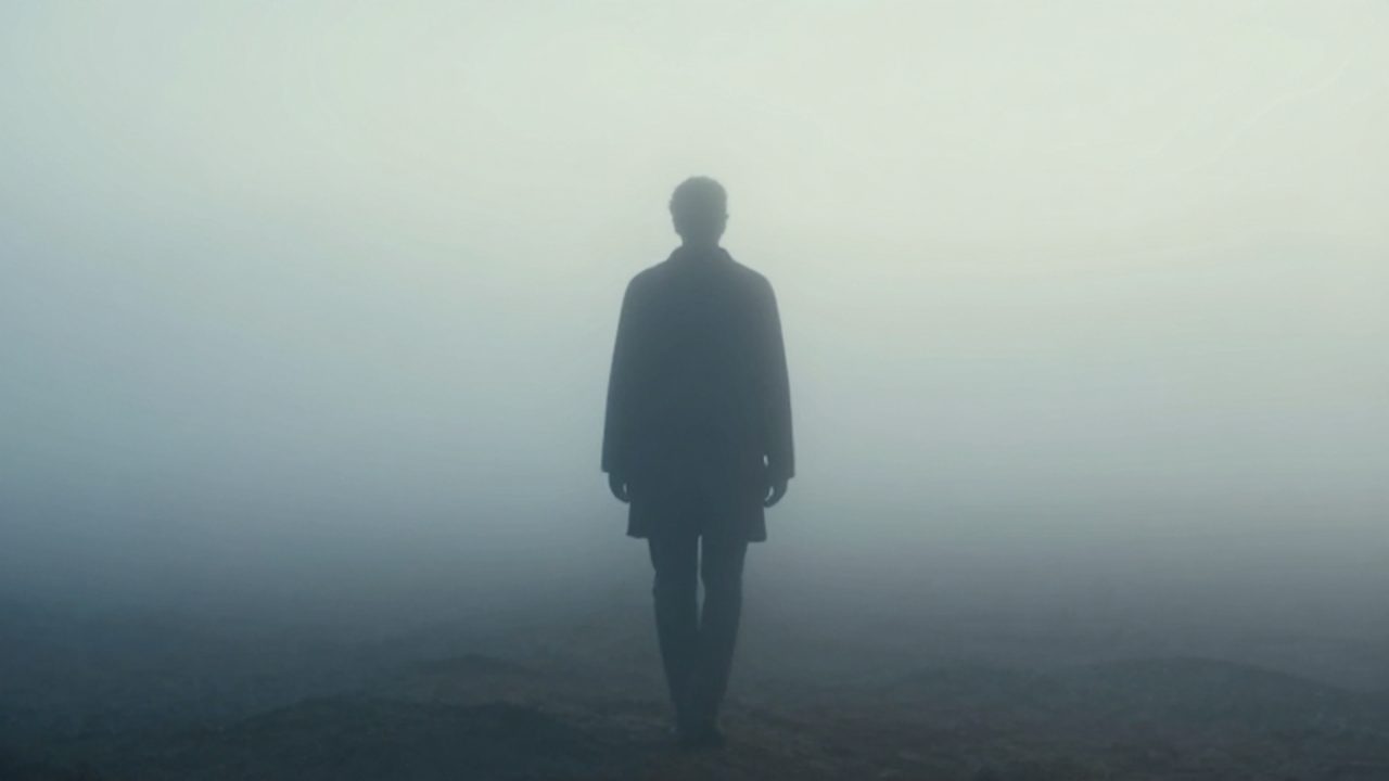 Silueta borrosa y misteriosa de un desconocido caminando entre una densa niebla en un paisaje onírico.