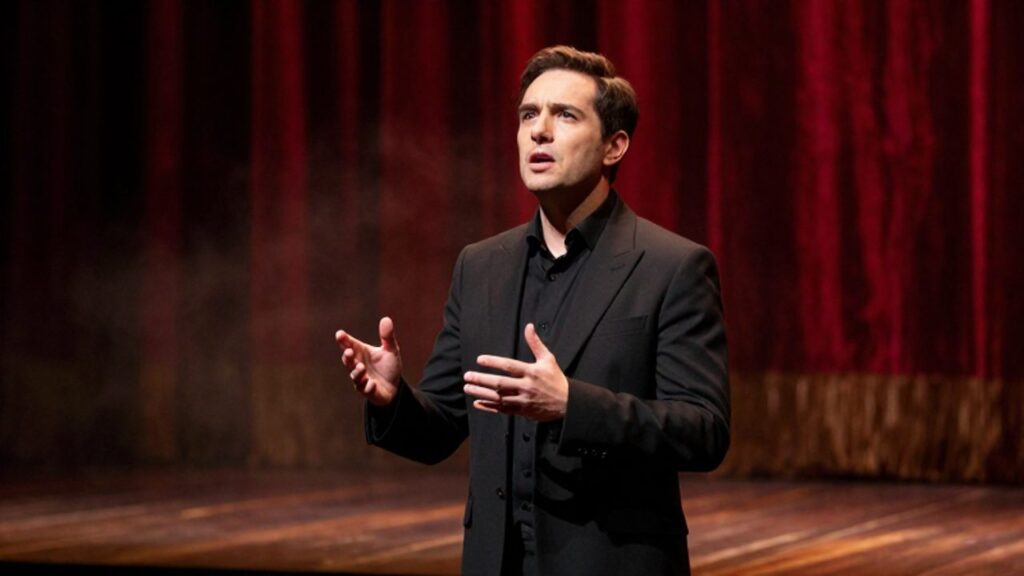 Actor realizando un monólogo dramático bajo un foco de luz sobre un escenario con cortinas rojas de fondo.