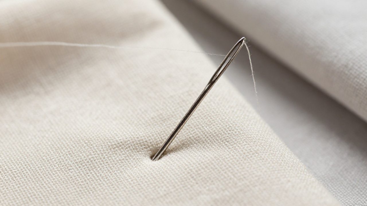 Aguja de metal atravesando una tela de lino para crear un pequeño agujero.