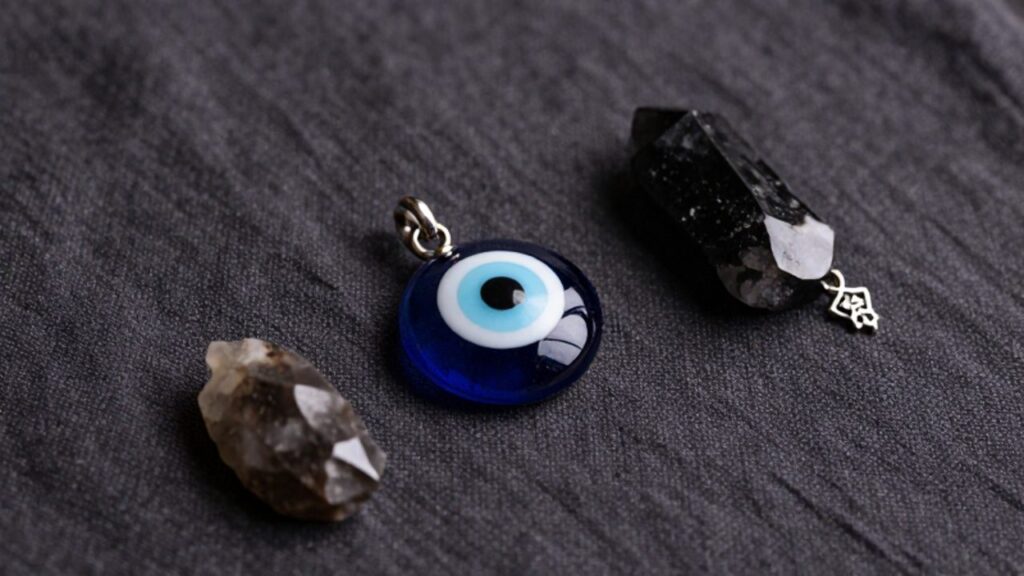 Un ojo turco de cristal azul, una piedra de turmalina negra y un amuleto de la mano de Fátima dispuestos sobre una tela oscura.