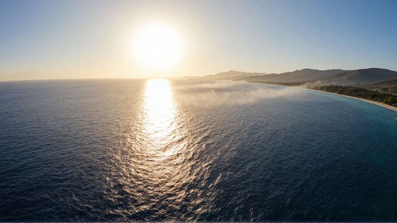 Vista aérea de un sol intenso sobre un océano azul profundo con montañas al fondo.