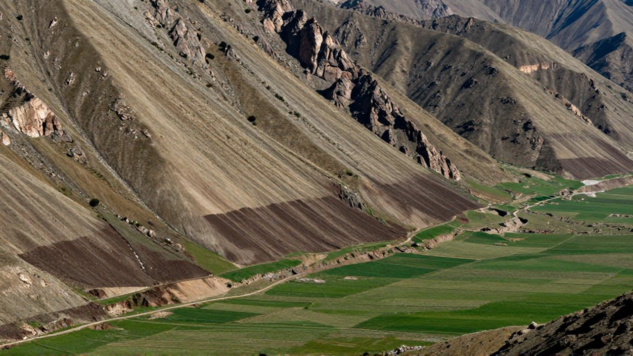 Corte transversal de una montaña rocosa que desciende hacia un valle de suelo fértil y verde.